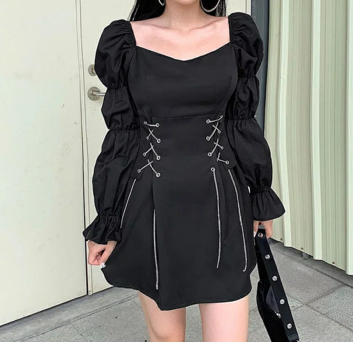 Person wearing a black dress with puff sleeves and lace-up details, standing against a neutral background.