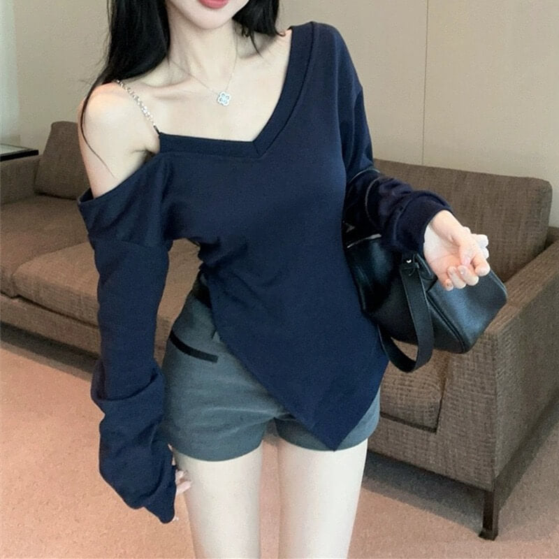 Woman wearing a navy blue oversized sweater over a black top with denim shorts, holding a black handbag indoors.