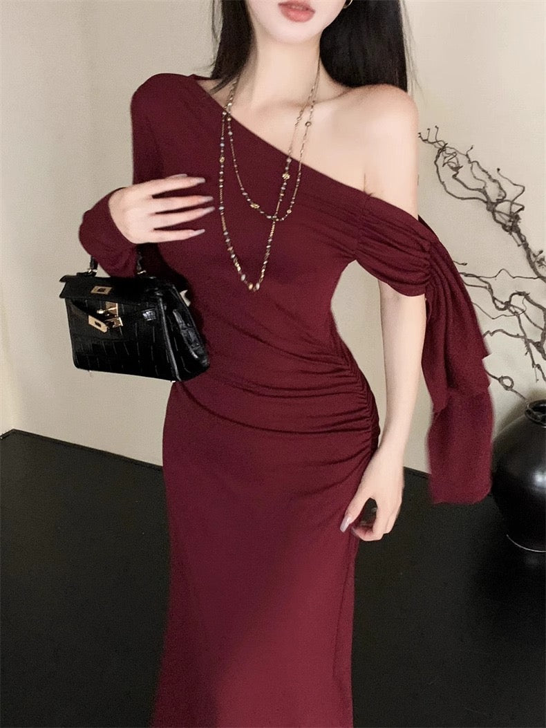 Woman wearing a burgundy one-shoulder dress holding a black handbag indoors.